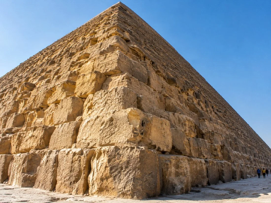 Die reuse kalksteenblokke aan die basis van die Groot Piramide van Khufu, met klein figuurtjies van besoekers vir skaal
