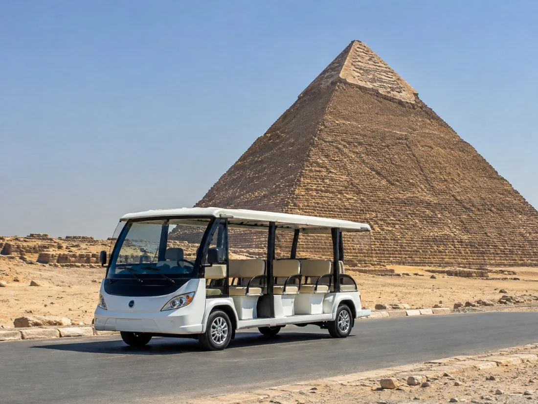 ’n Wit elektriese pendelbus op die pad oor die Giza-plato met die Groot Piramide agter