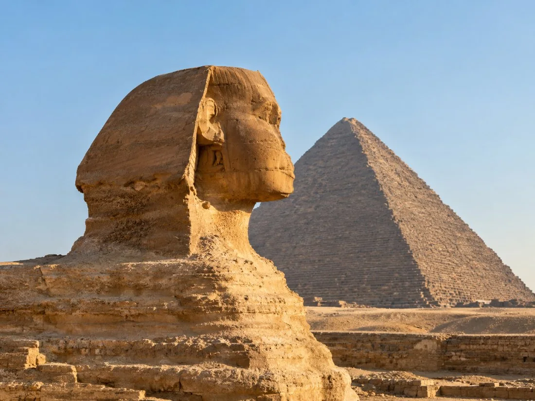 Die Groot Sfinks van Giza in profiel in warm oggendlig, met die Piramide van Khafre wat agter dit opry